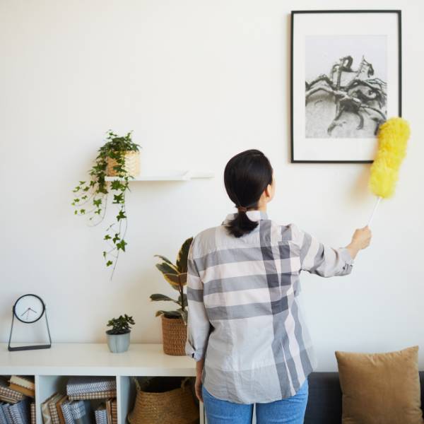 A professional house cleaner dusting a framed photo hanging on a wall.